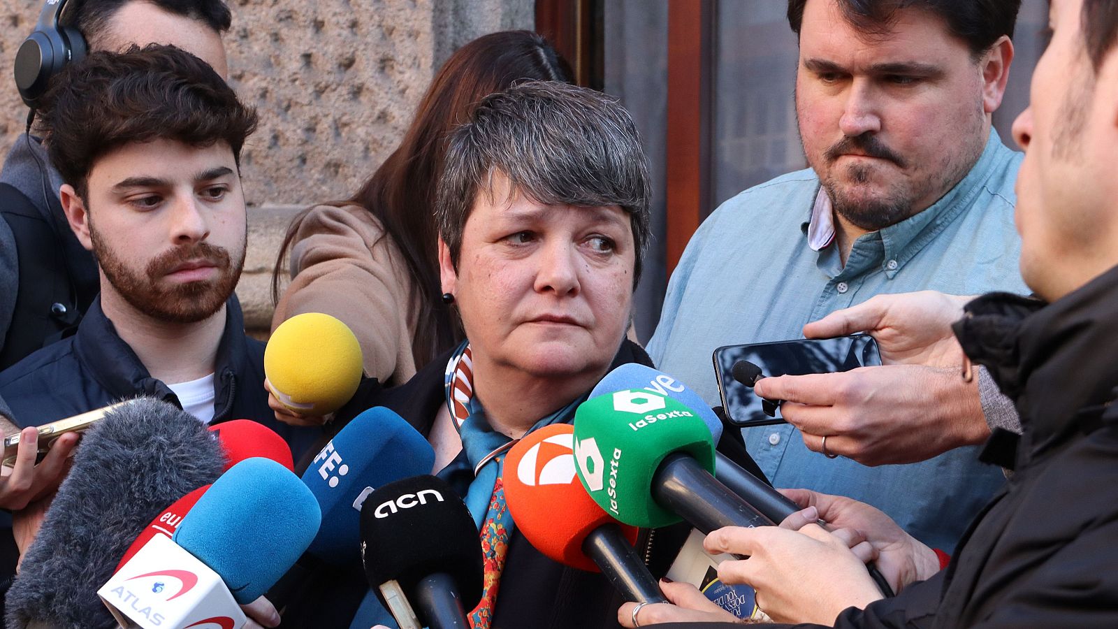 Abogada seria con el pelo corto y canoso, da declaraciones a la prensa rodeada de micrófonos de diferentes medios de comunicación.