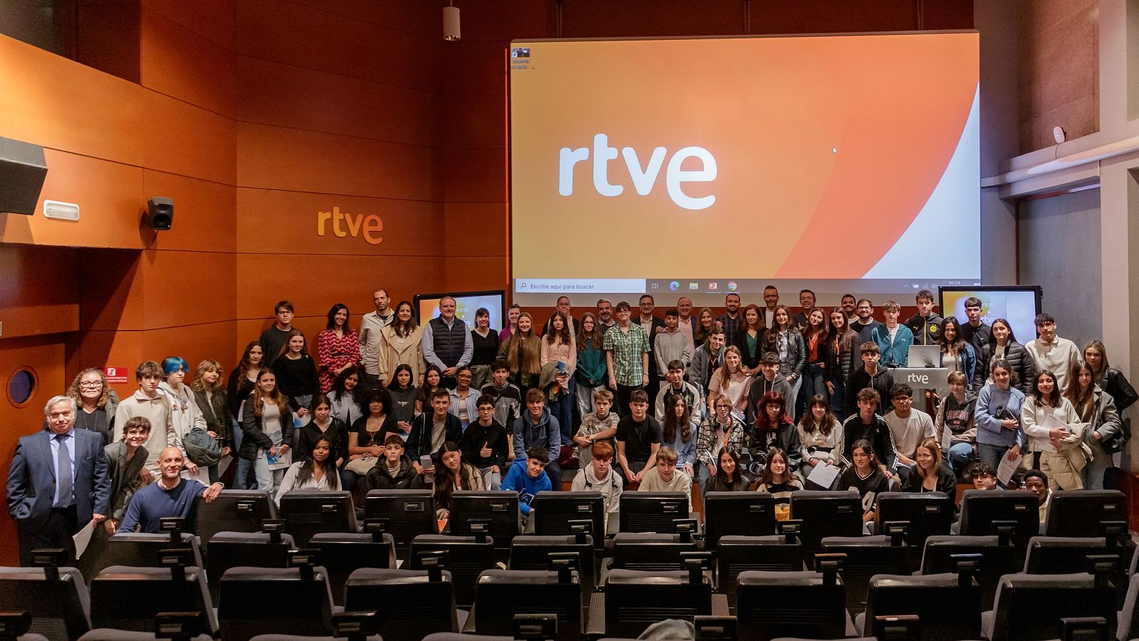 Grupo numeroso de jóvenes, algunos sentados y otros de pie, posan para una foto con el logotipo de RTVE visible en el fondo.  Posible evento de un programa audiovisual.