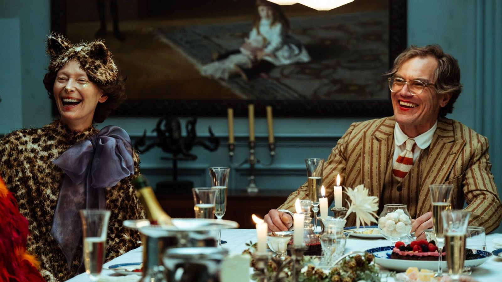 Cena festiva en un comedor elegante: una mujer con sombrero de orejas de gato y un hombre en traje disfrutan de una comida con champán y pastel.