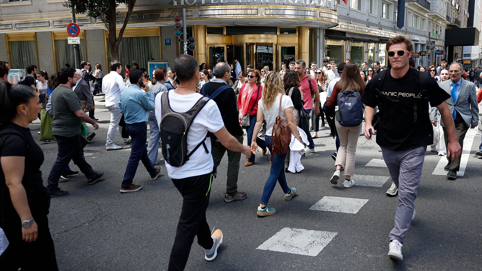 Peatones cruzan la Gran Vía de Madrid durante un apagón, frente al Hotel Emperador.  La ausencia de vehículos y la ropa de entretiempo de los peatones son detalles destacables.