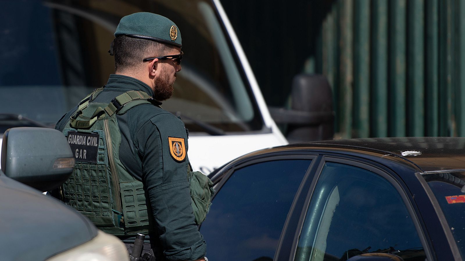 Un Guardia Civil rodeado de coches mira atentamene hacia la puerta de un edificio