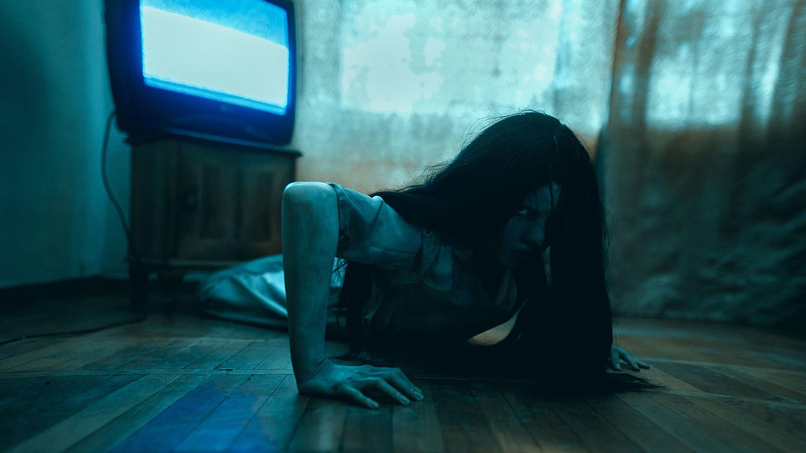 Mujer con cabello oscuro arrastrándose, expresión de terror, televisor antiguo al fondo, atmósfera de película de terror.