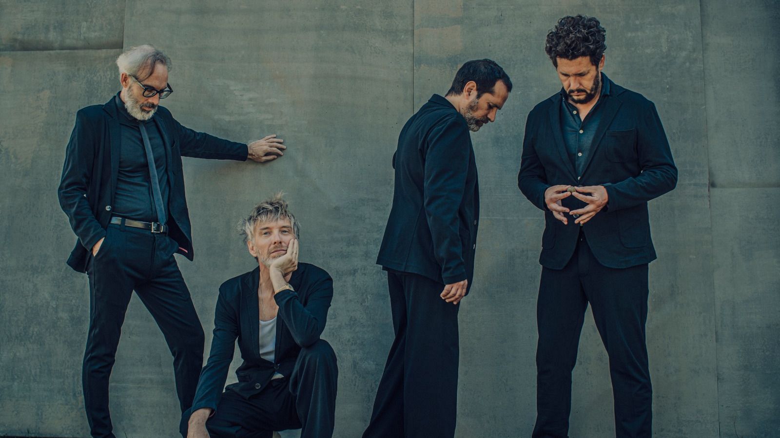 Cuatro músicos posan juntos, vestidos de negro sobre un fondo gris.  Varias poses y expresiones individuales.