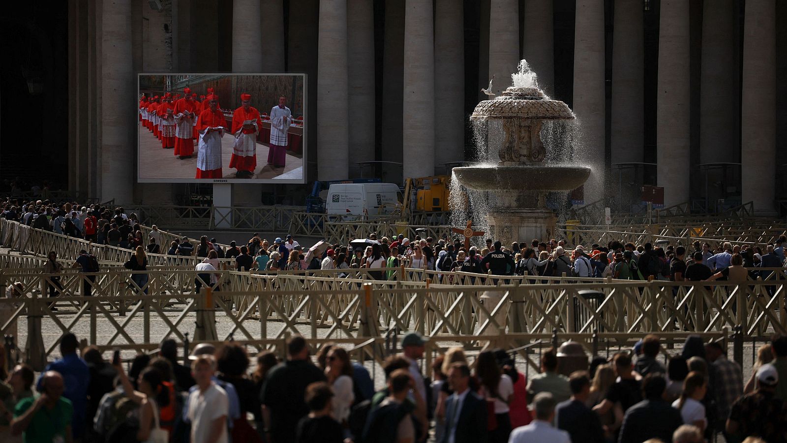 La gente hace cola para entrar en la Basílica de San Pedro en el Vaticano, en el primer día del cónclave para elegir al nuevo Papa, mientras los cardenales se muestran en una pantalla