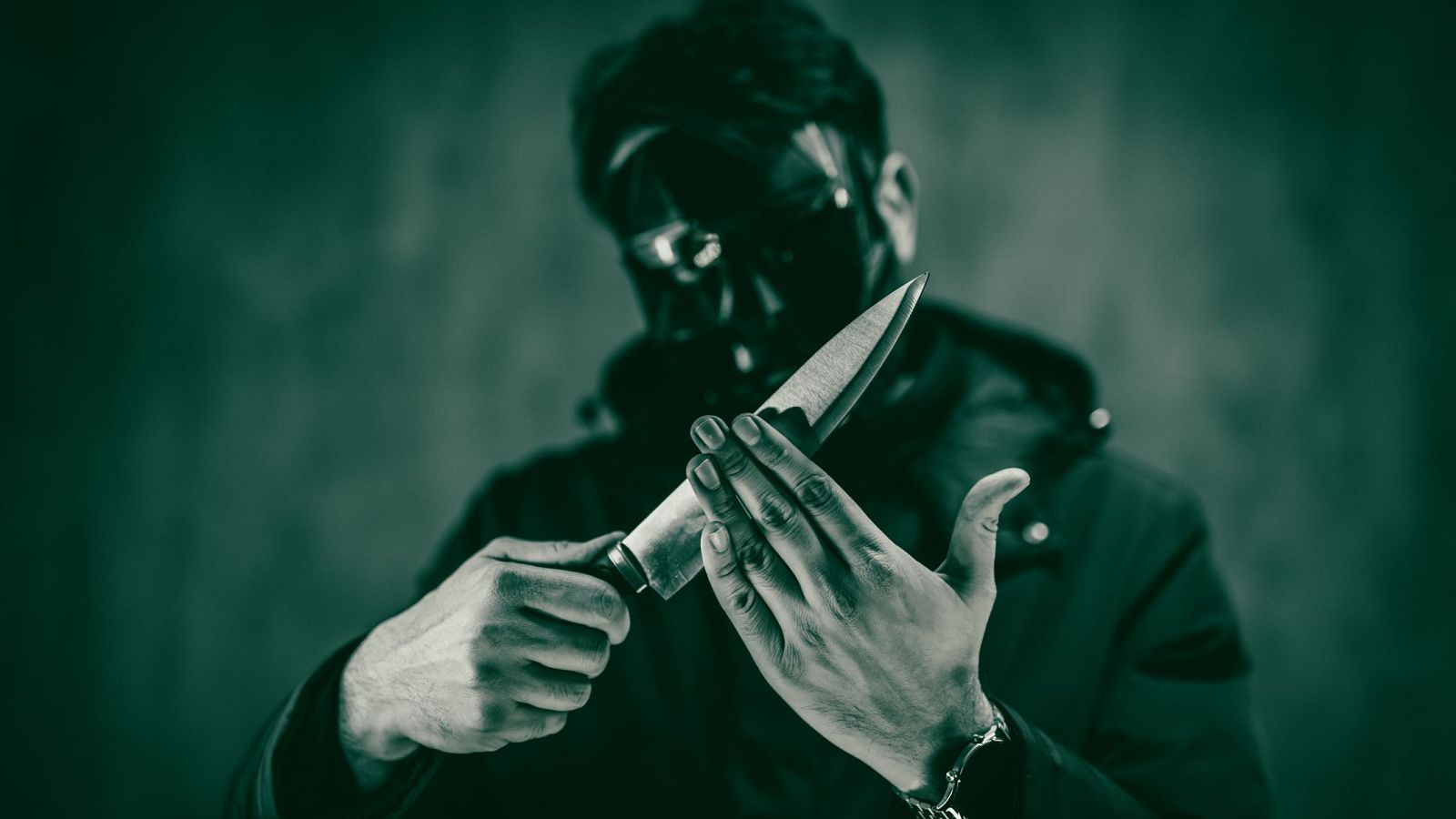 Imagen en blanco y negro de una persona enmascarada con cuchillo, creando una atmósfera amenazante.  El fondo es oscuro y la hoja del cuchillo apunta hacia arriba.