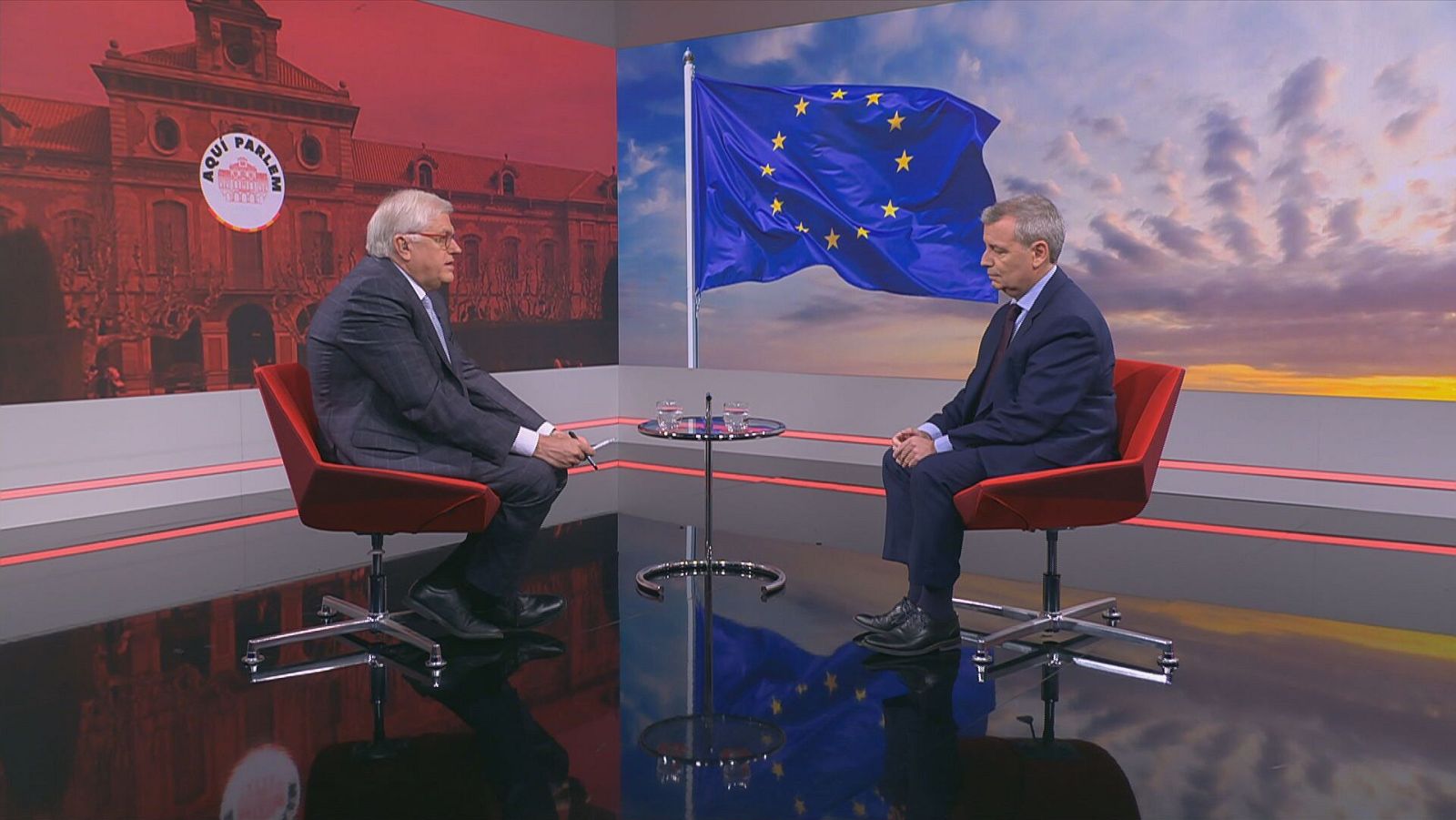 Lluís Falgàs i Jordi Xuclà asseguts a les cadires al plató del programa, amb una bandera europea de fons a la pantalla