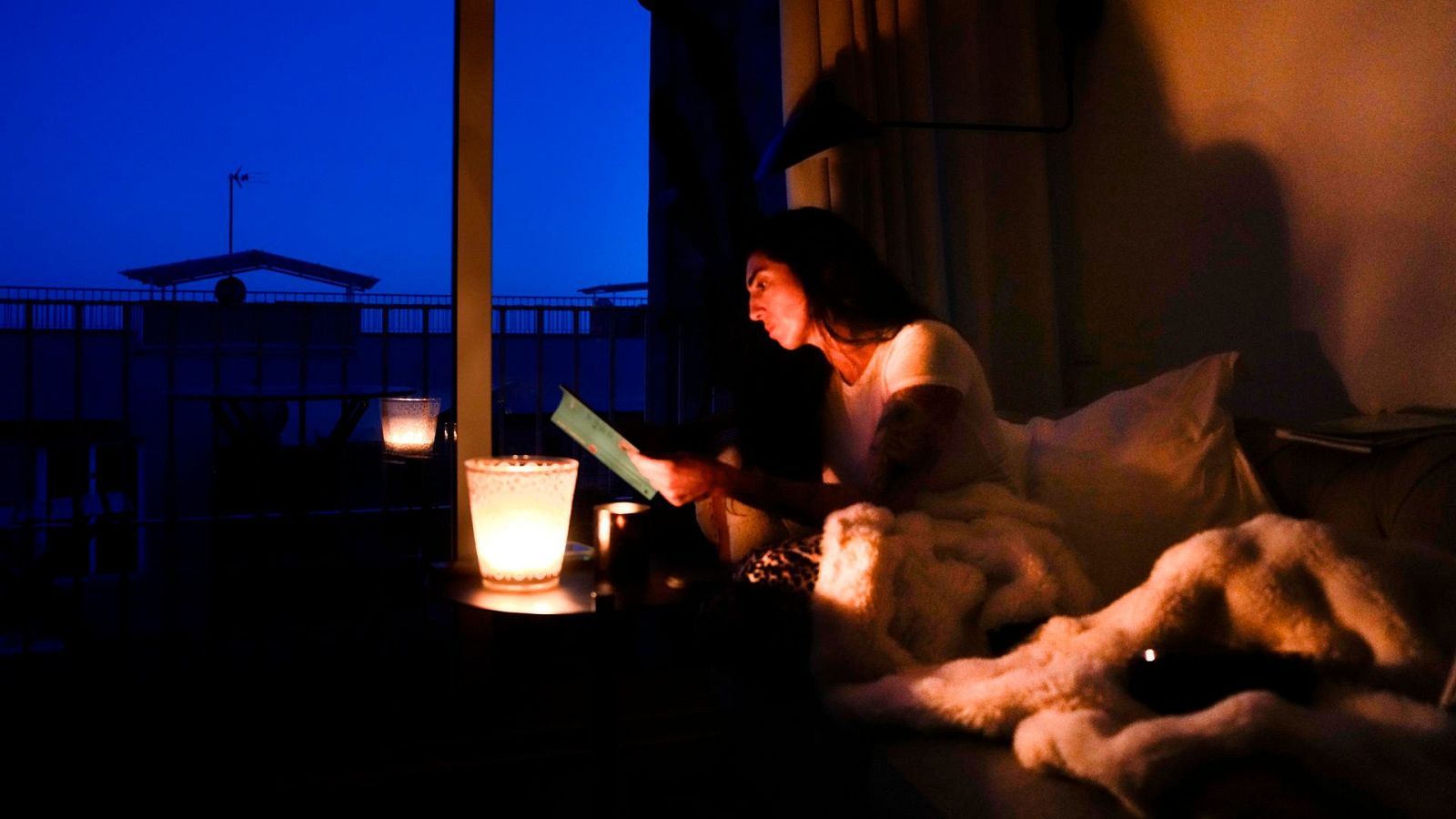 Encuesta sobre el apagón del 28 de abril: una mujer lee en su casa con ayuda de una vela.