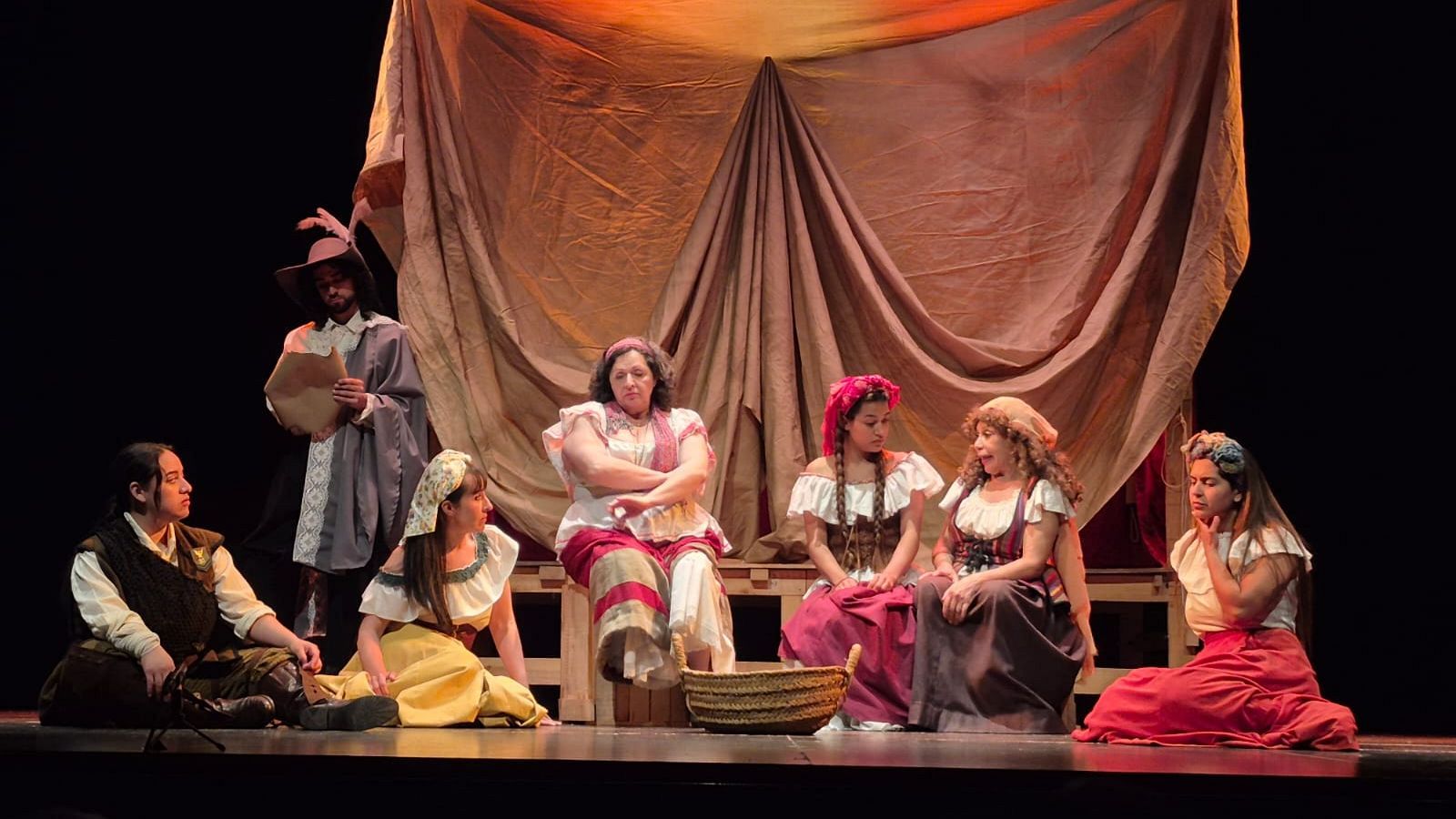 Actores ensayando 'Soldadescas' en un escenario con telón marrón. Vestuario medieval/renacentista. Una cesta de mimbre en el centro.