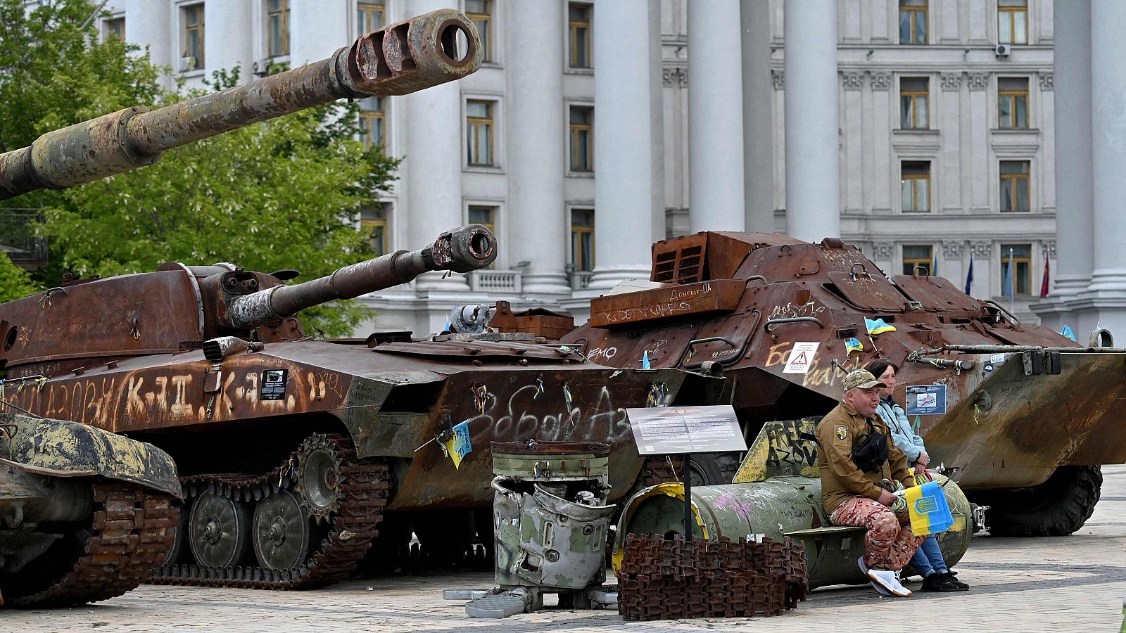 Un voluntario vende banderas ucranianas mientras está sentado sobre un fragmento de un misil en el museo al aire libre de equipo militar ruso destruido