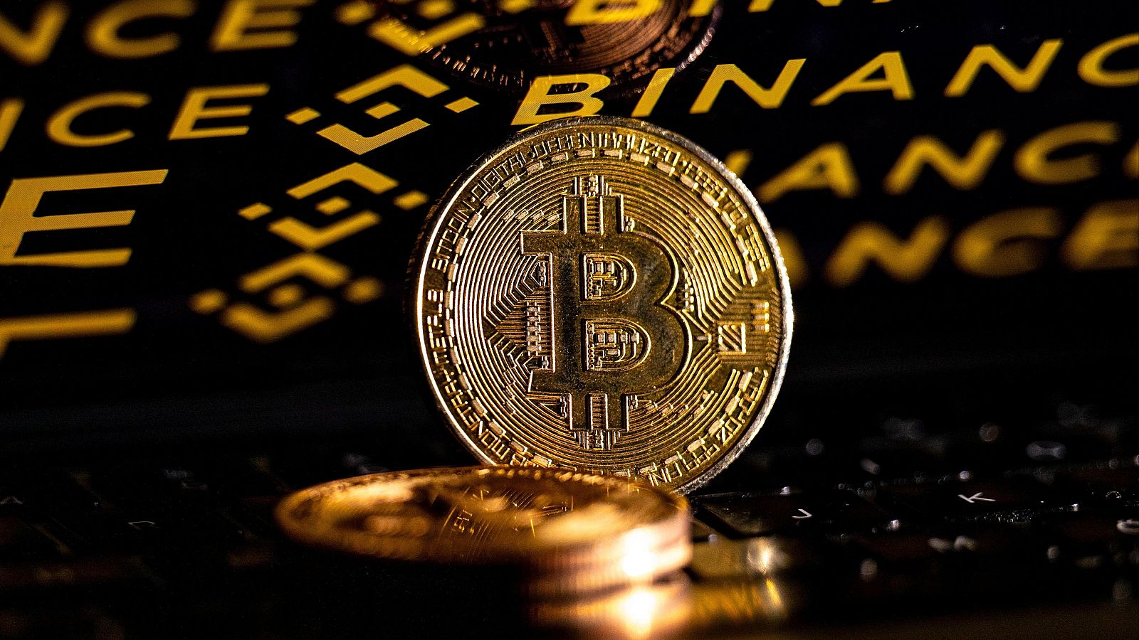 Monedas de Bitcoin frente a una pantalla con el logotipo de Binance
