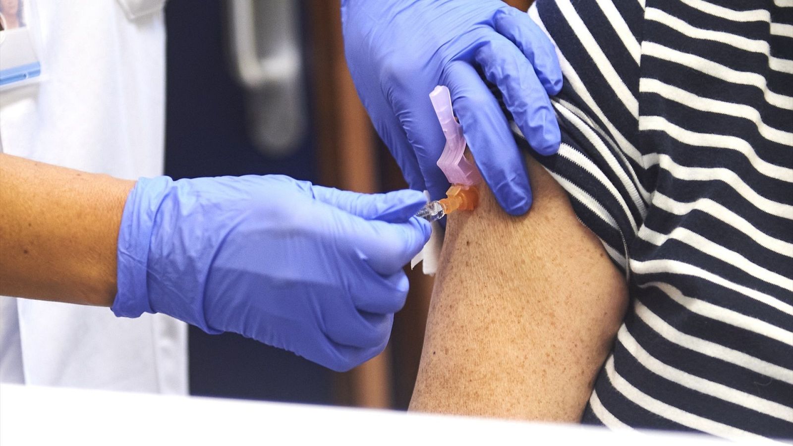 Vacunación contra la gripe: enfermera inyecta a una mujer con camiseta a rayas.  Se observa la aguja en el brazo de la paciente.