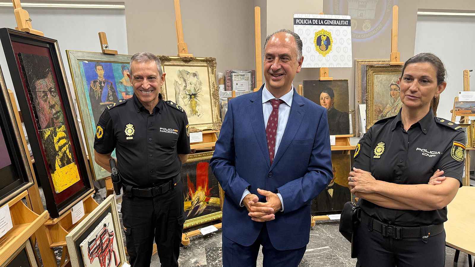 Incautación de obras de arte: dos policías y un civil en una sala con pinturas en caballetes.  Posible escena en un depósito policial o espacio expositivo.