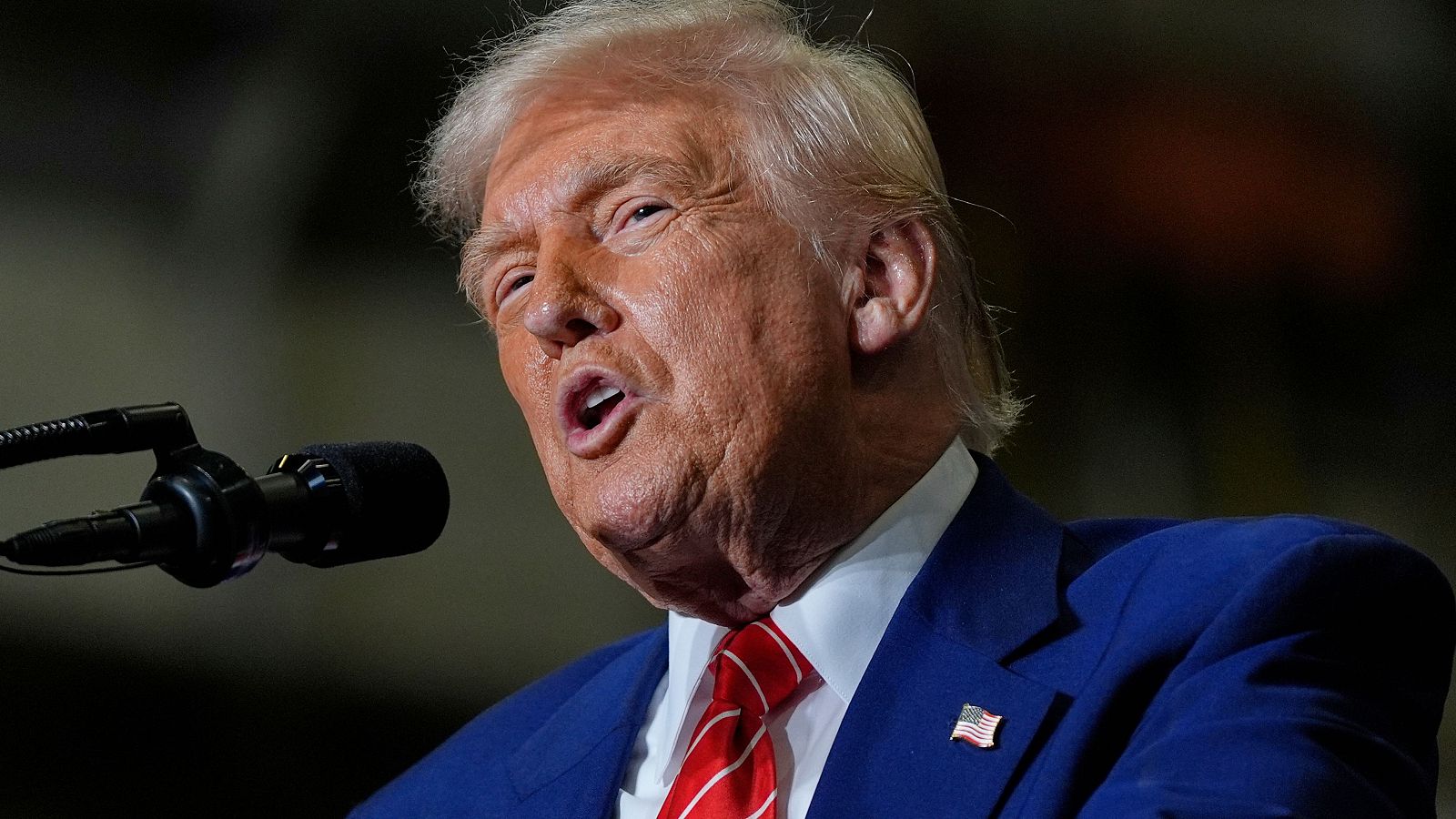 El expresidente Trump, en traje azul oscuro y corbata roja, ofrece un discurso ante un micrófono.