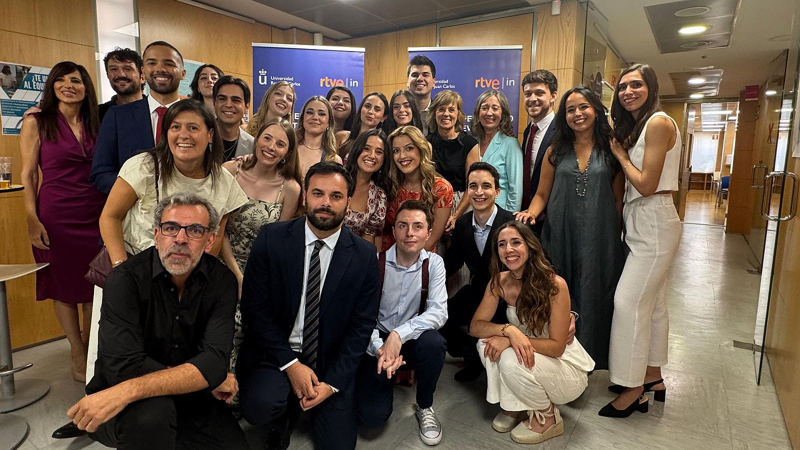 Graduados de un Máster de Periodismo de Televisión posan sonrientes en una foto de grupo tras la clausura.  Ambiente formal, interior.