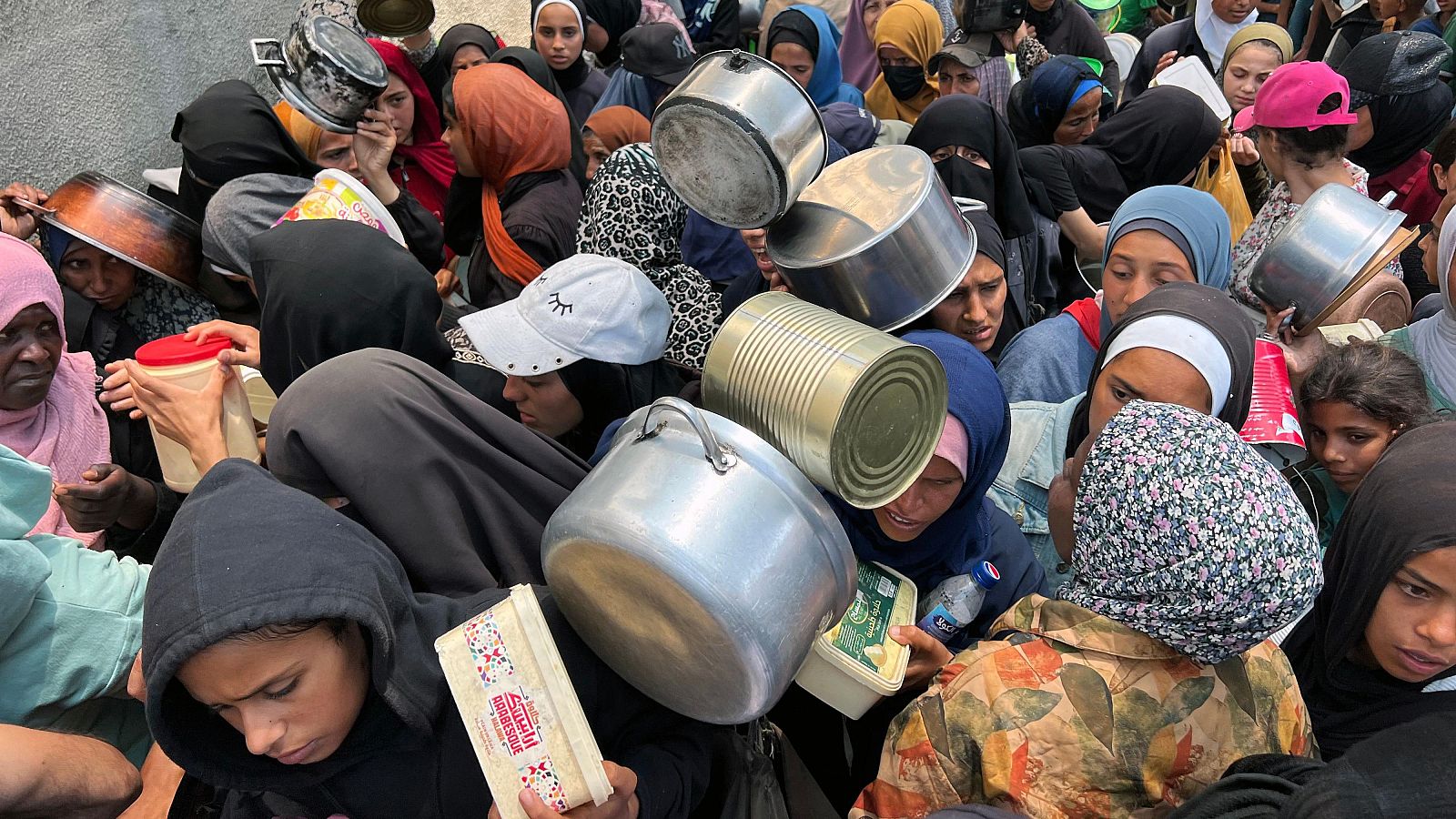 Decenas de personas esperan con ollas y recipientes para recibir ayuda en el campo de refugiados de Nusairat