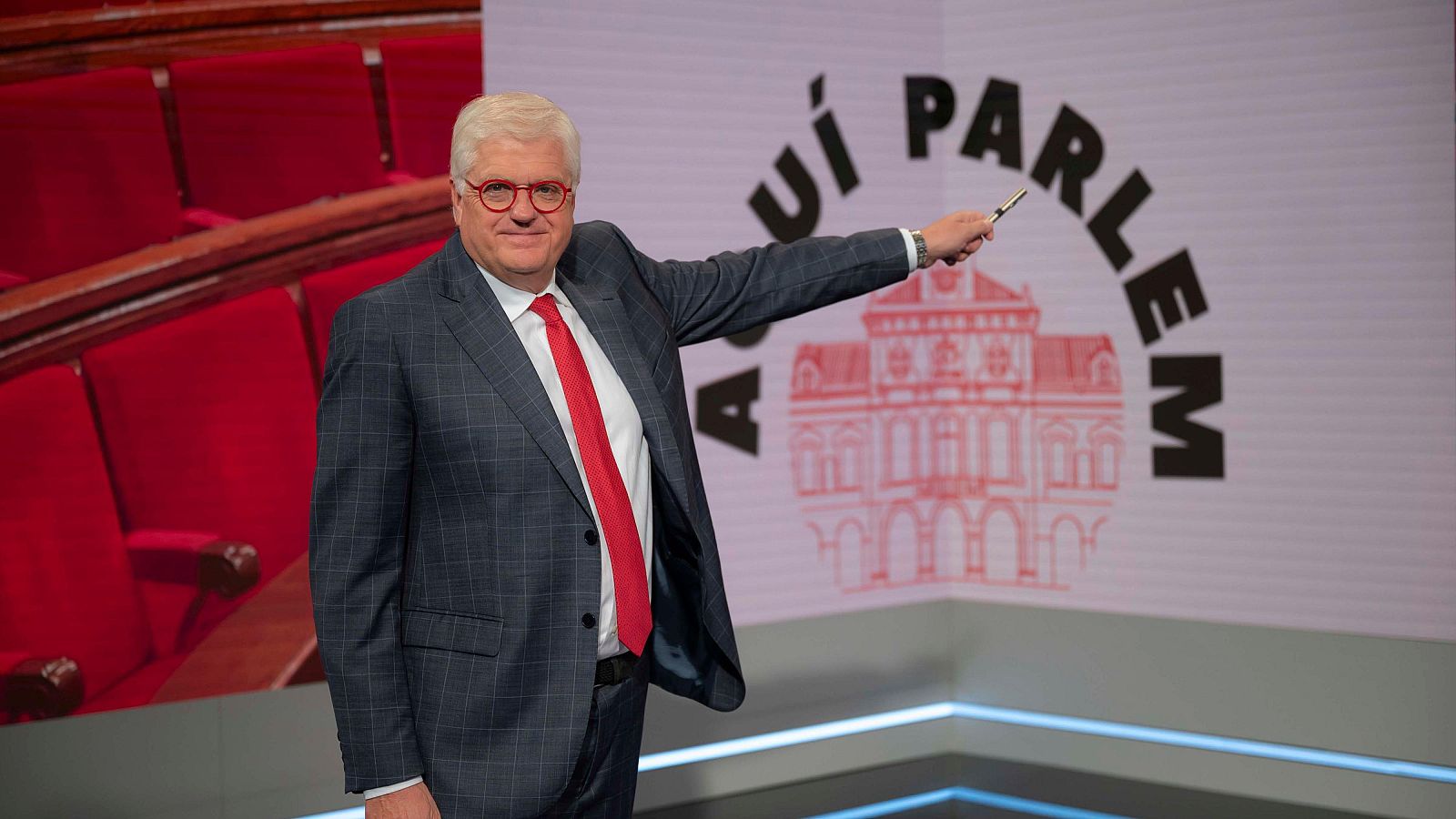 Lluís Falgàs, presentador i director d''Aquí Parlem', en el plató del programa assenyalant el logotip.