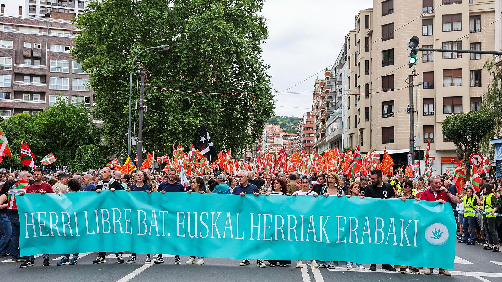 Manifestación callejera con pancarta en euskera y numerosas banderas vascas.  Participantes reclaman el derecho a decidir.