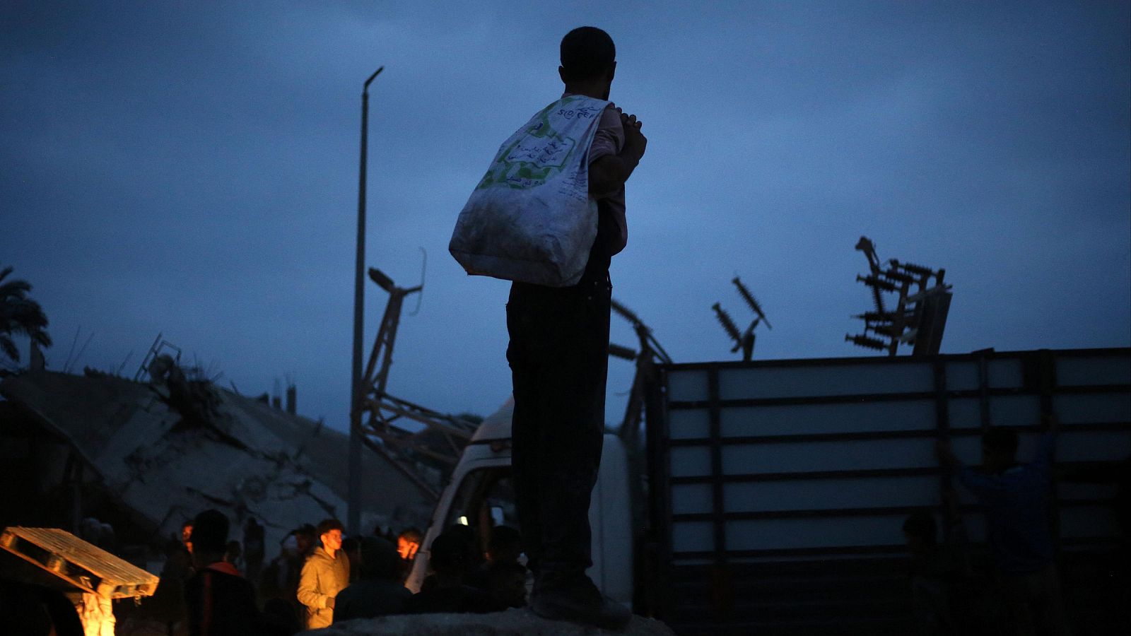 Un joven palestino lleva una bolsa de ayuda humanitaria observa cómo la gente llega a un punto de distribución en el campamento de Bureij para refugiados palestinos