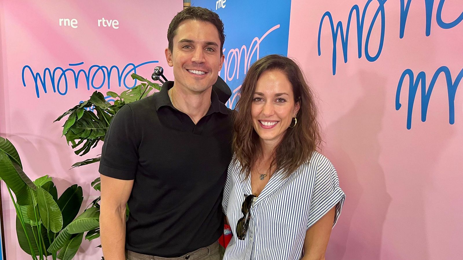 Dos actores sonríen a cámara en una foto promocional. Él lleva polo negro y pantalones marrones; ella, blusa a rayas. Fondo con logo de RNE y RTVE, y el título 'Mañana'.