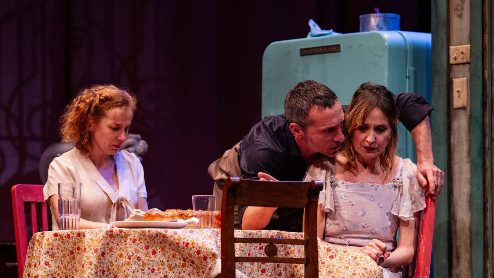 Nathalie Poza, Pablo Derqui y María Vázquez interpretan una escena con tensión en un ambiente evocador de época pasada, con una mesa, comida y una nevera antigua.