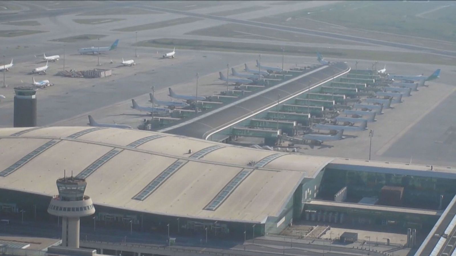 Imagen aérea de un aeropuerto activo: aviones en pistas, terminal, torre de control y señalización visible.