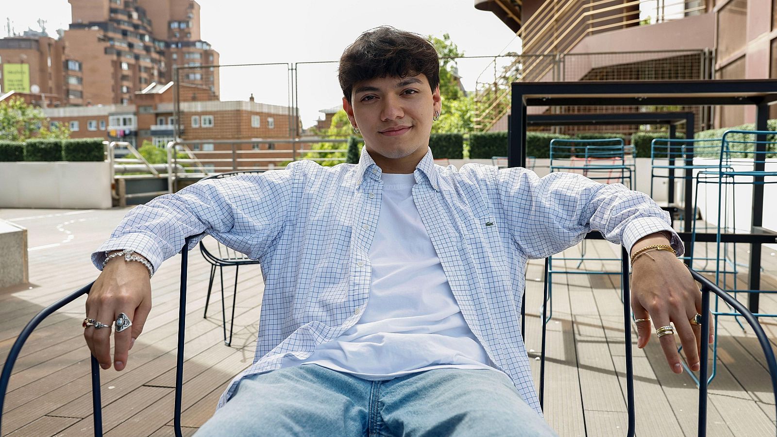 Contratenor filipino ganador de Eurovisión 2025, con camisa de cuadros y vaqueros, sentado en una terraza, aspira a ganar un Grammy.