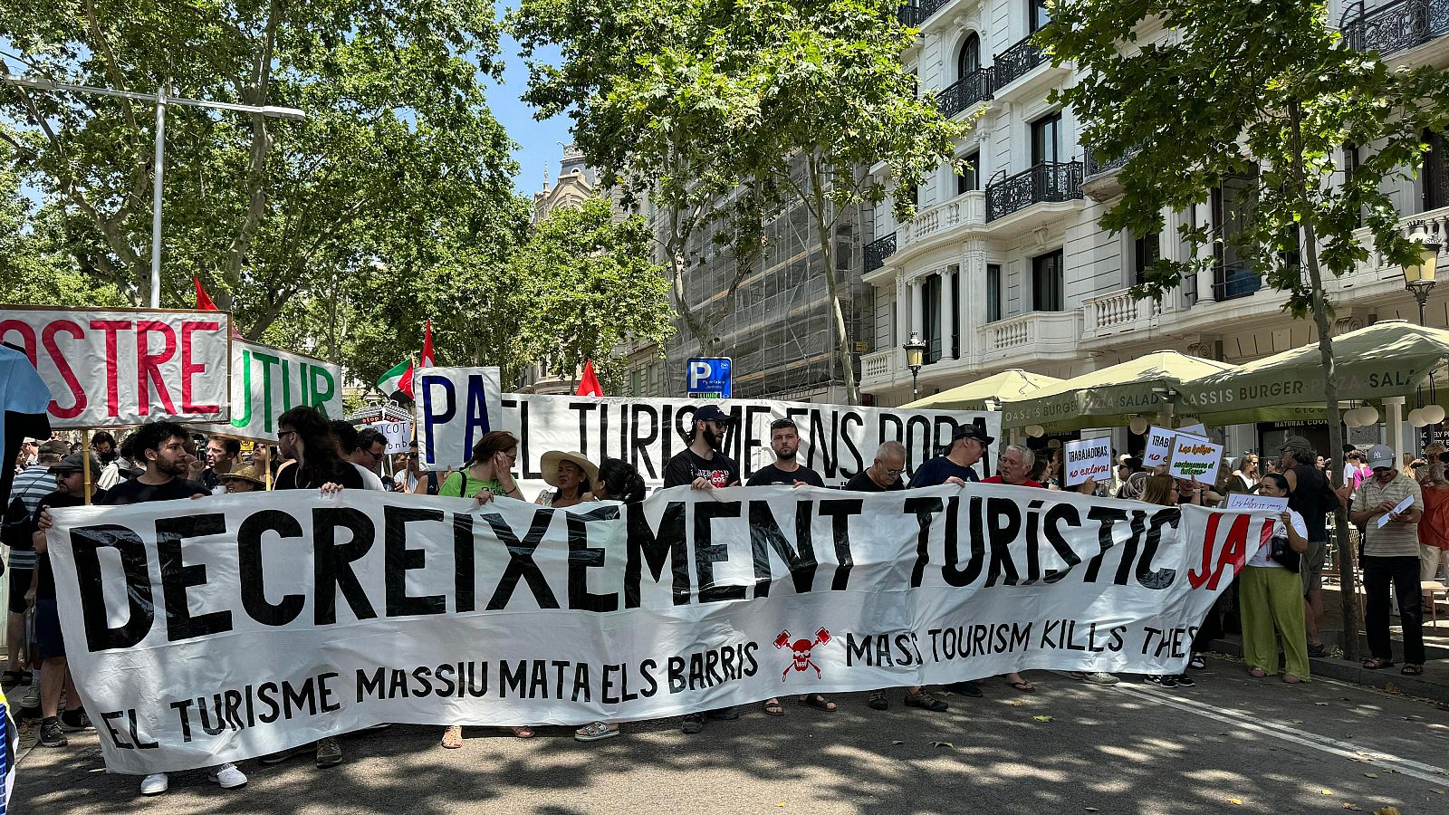 Manifestación urbana contra el turismo masivo. Pancartas con lemas en catalán e inglés reclaman un decrecimiento turístico, denunciando el impacto negativo en los barrios.