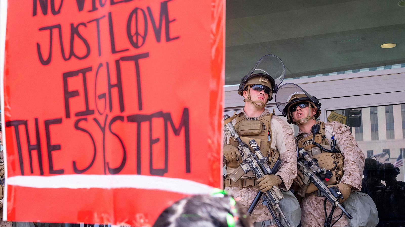 Dos marines estadounidenses junto a una pancarta con la frase "sin violencia, solo amor, lucha contra el sistema"