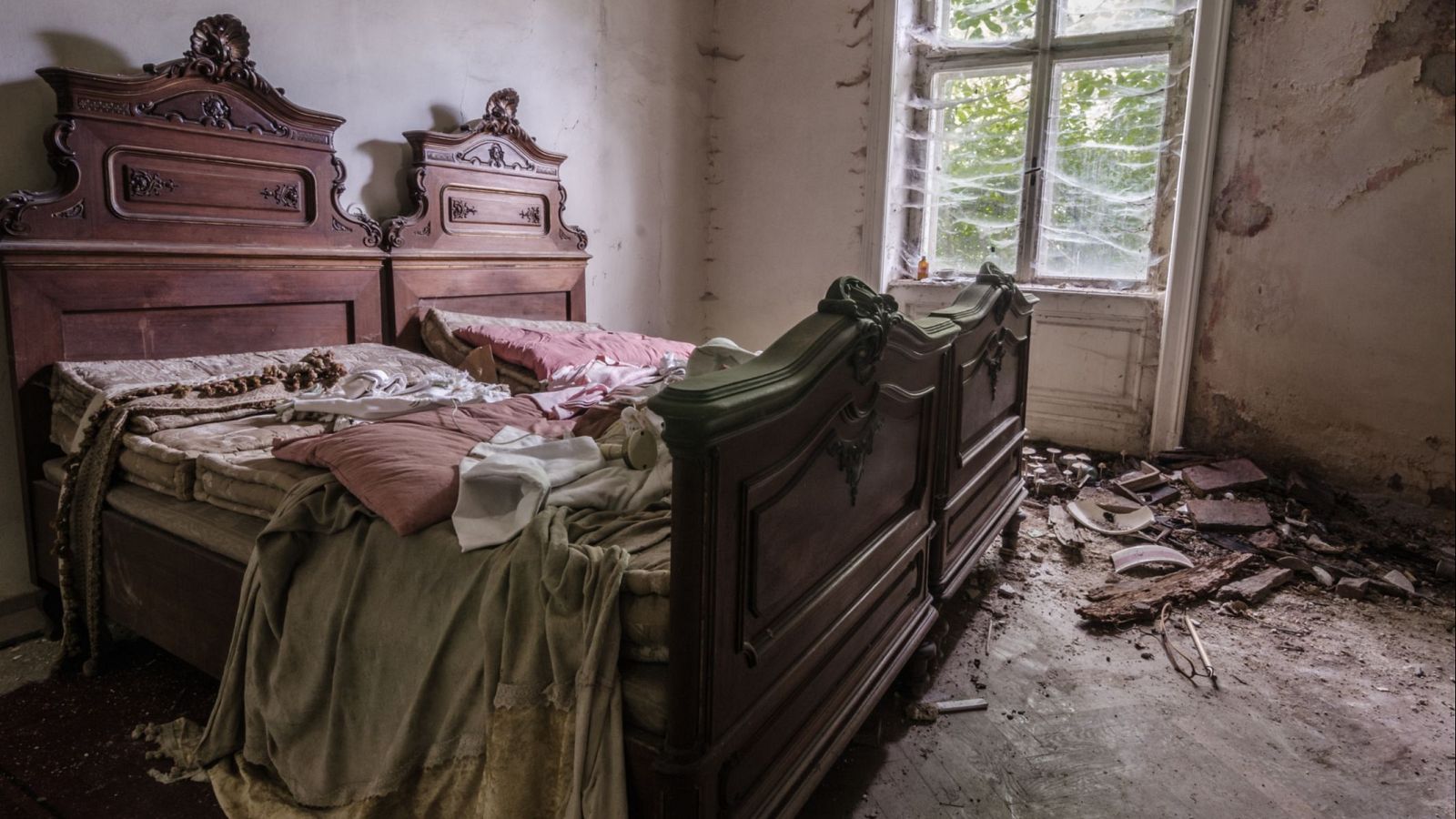 Dos camas deshechas en una habitación ruinosa con escombros en el suelo y una ventana entelañada. Ambiente sombrío y misterioso.