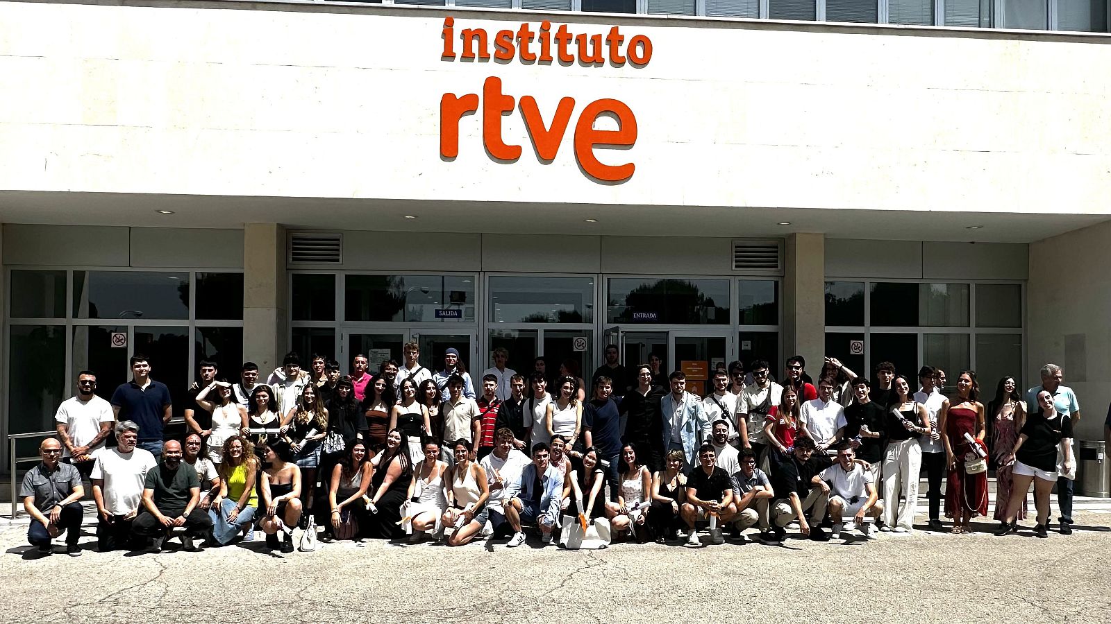 Grupo de jóvenes, vestidos informalmente, posan para una foto de graduación.  Algunos están de pie, otros sentados. Promoción 2025.