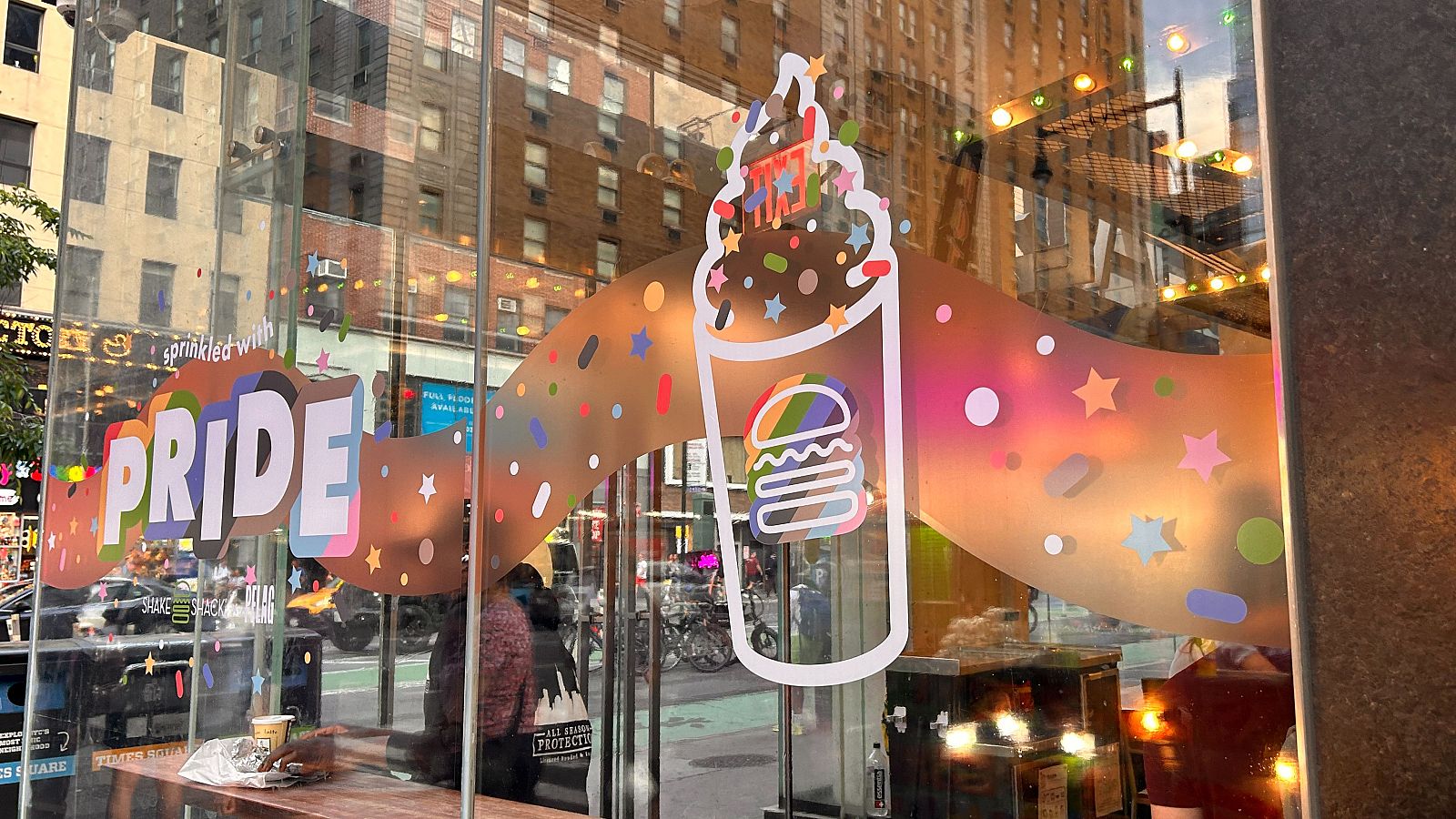 Escaparate con decoración del Orgullo LGBTIQ+, mostrando la frase "sprinkled with PRIDE" en letras arcoíris sobre un dibujo de un batido y una hamburguesa.