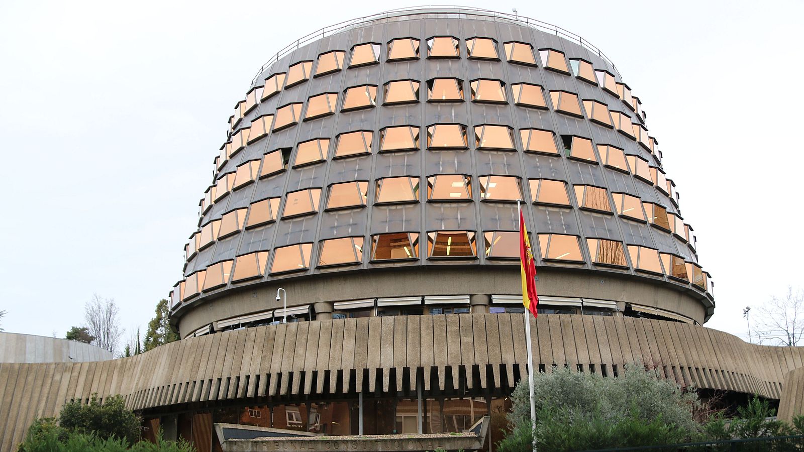 Edificio cilíndrico con cúpula de ventanas trapezoidales, bandera española y vegetación. Fotografía tomada al mediodía por Miquel Vera para la ACN.