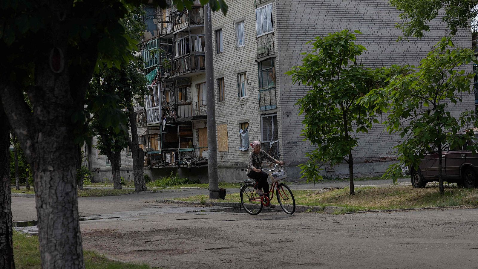 Una mujer pasea en bicicleta junto a un edificio residencial dañado