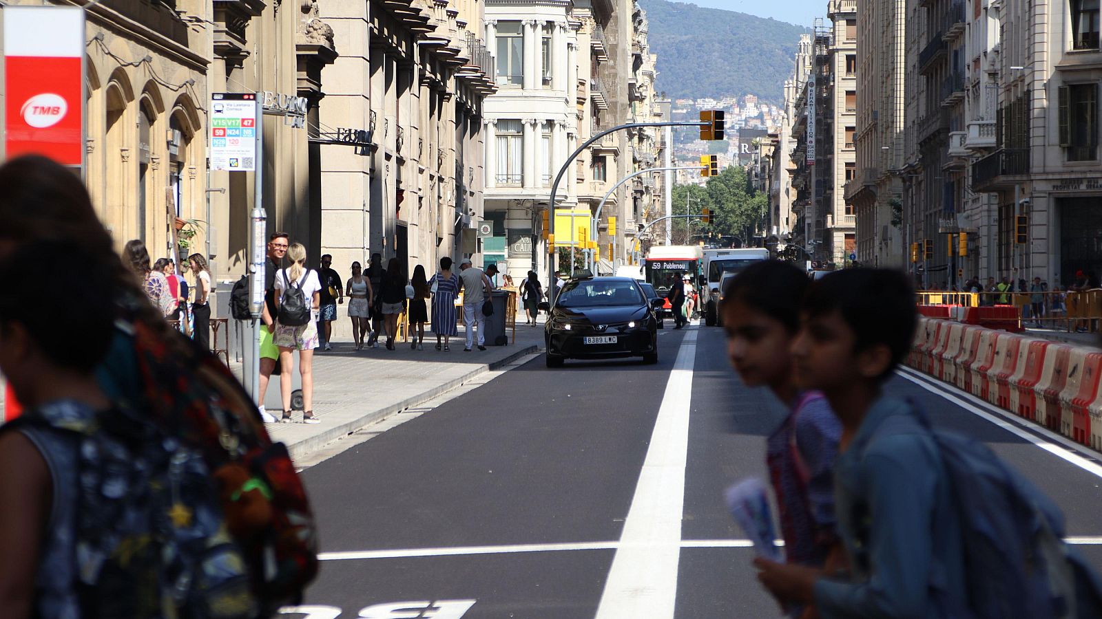 Diversos vehicles baixen per la Via Laietana mentre vianants creuen un pas de zebra.