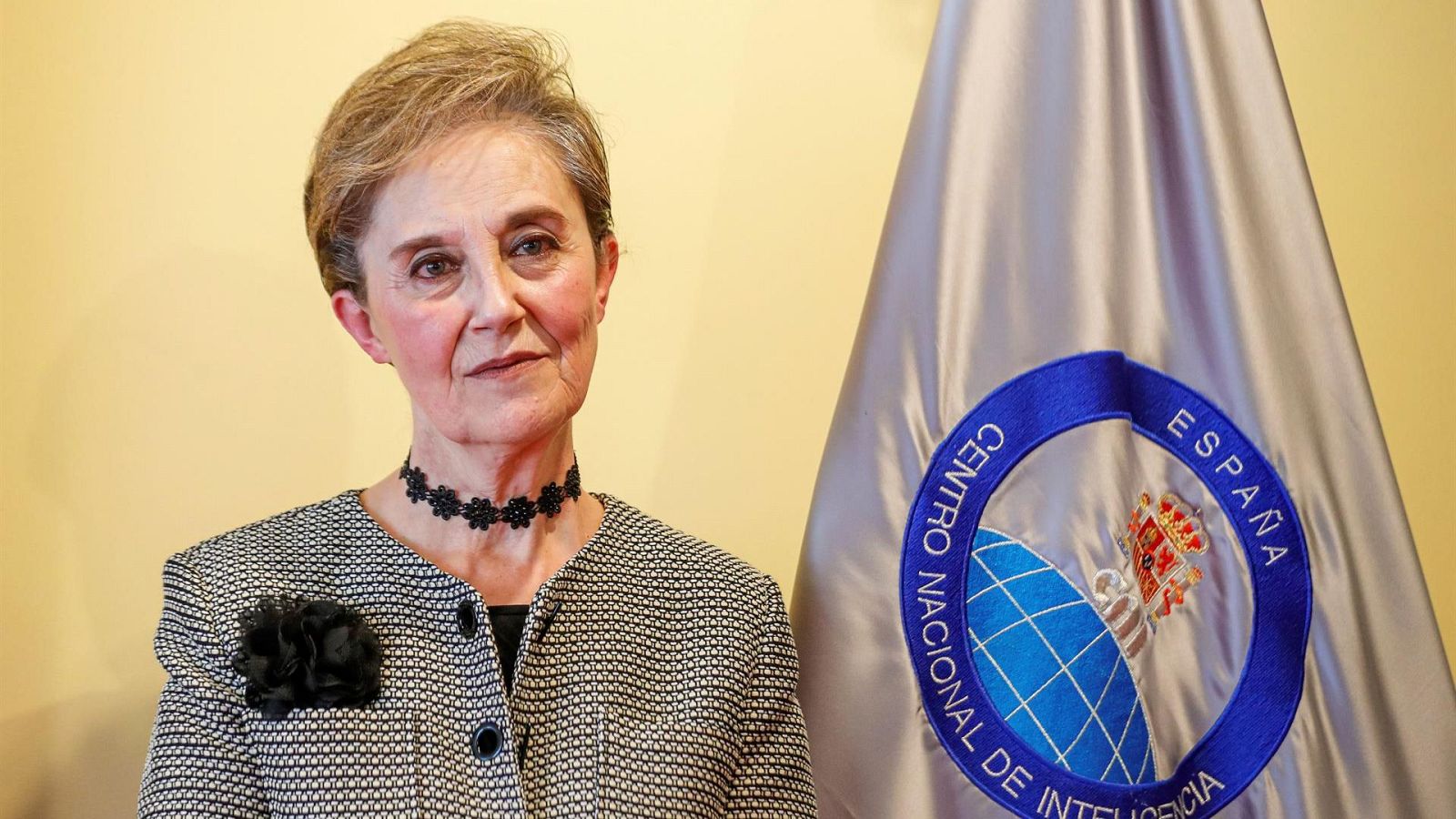 Paz Esteban, en su nombramiento como directora del CNI. Viste chaqueta gris clara con broche negro, tras ella la bandera del CNI.