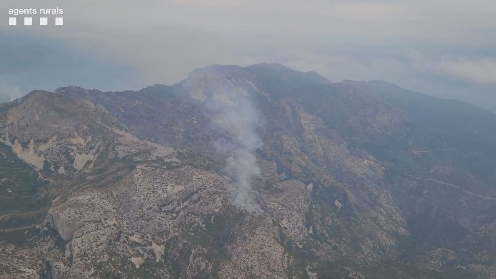 Incendio forestal en zona montañosa con abundante humo visible desde el aire.  Terreno rocoso y vegetación seca.