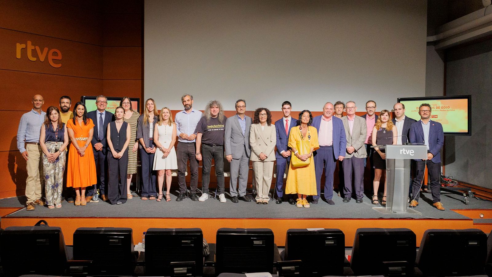 Grupo de personas en un escenario con logo RTVE, frente a una pantalla mostrando una presentación sobre 'Discursos de odio'. Auditorio con butacas visibles.