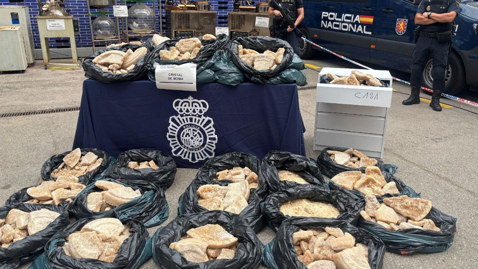 Incautación policial de droga: bolsas con sustancia beige clara, etiquetadas como "CRISTAL DE MOMA" y "CAJA", custodiadas por agentes uniformados.