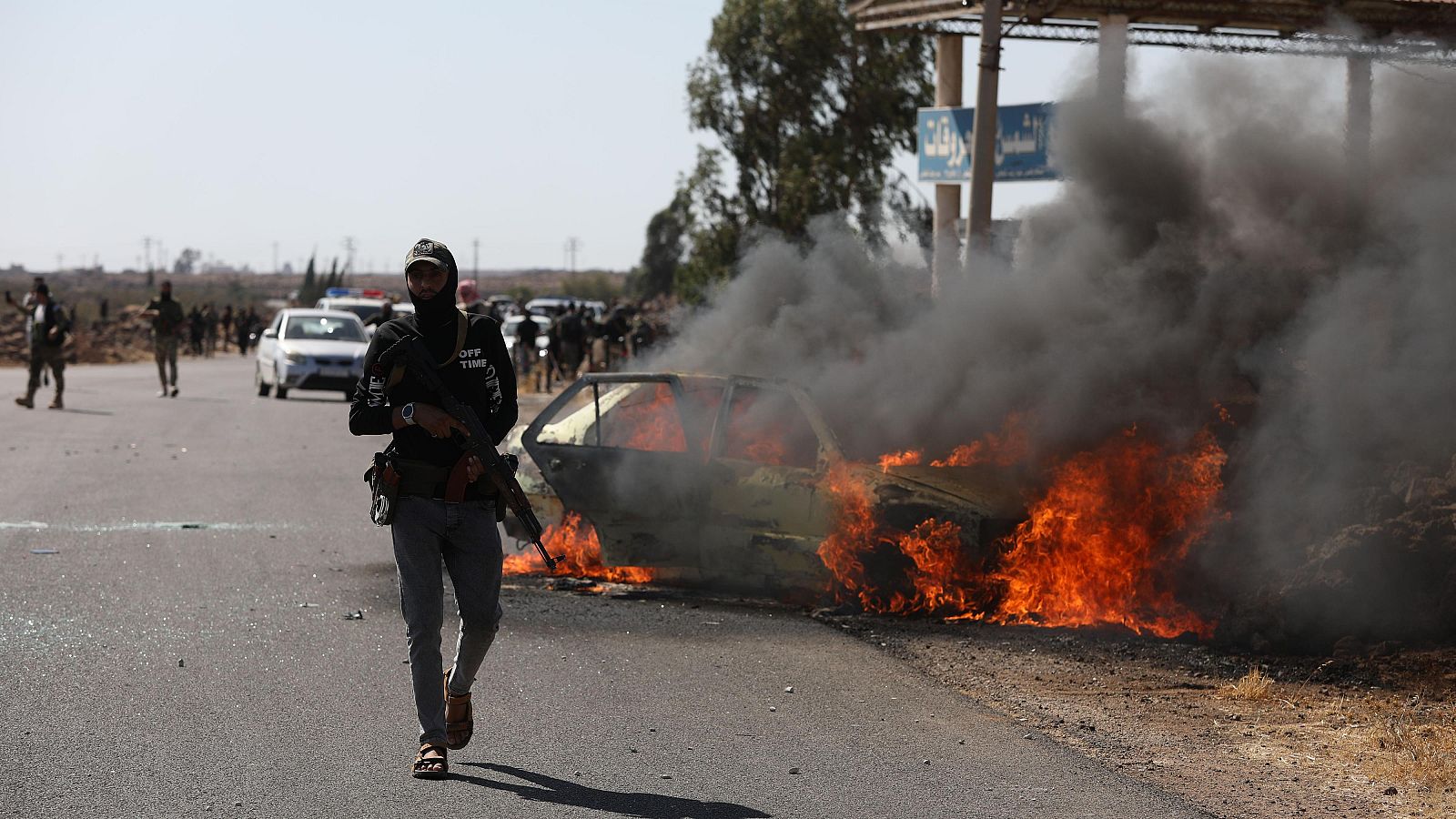 Hombres armados se ven cerca de un vehículo en llamas el 14 de julio de 2025, cerca de Sweida, Siria.