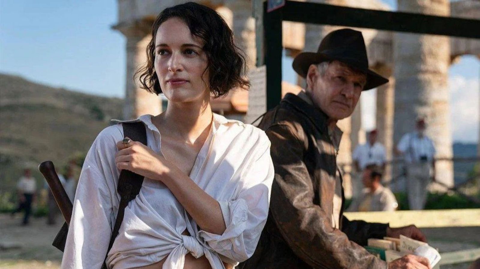 Phoebe Waller-Bridge e Indiana Jones (Harrison Ford) en una escena de la película, con atuendos de época y un fondo de ruinas antiguas.