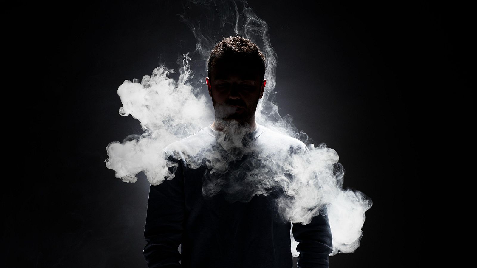 Figura envuelta en humo blanco sobre fondo negro.  El contraste y la oscuridad evocan misterio.