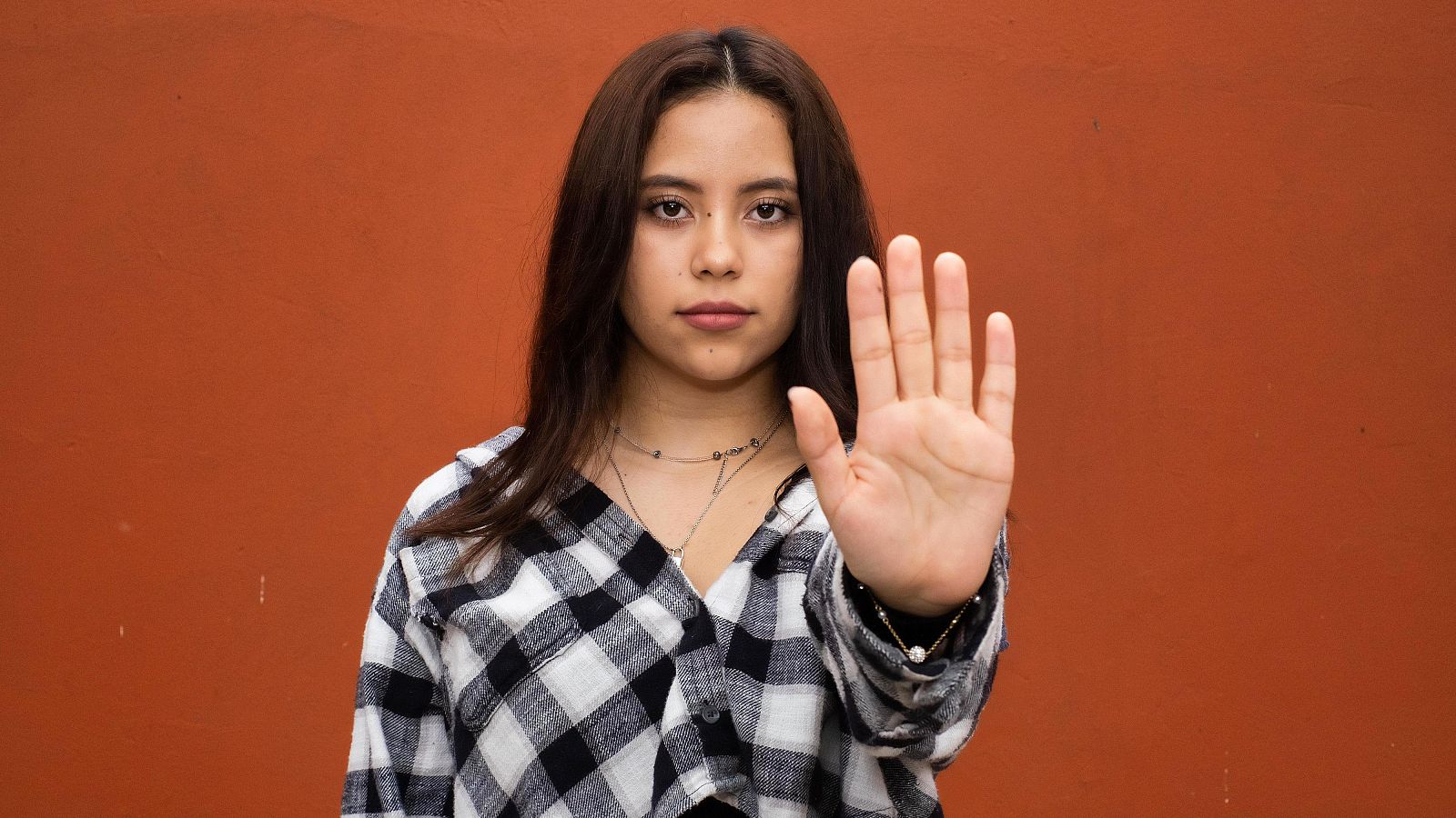 Una mujer latina joven mira a la cámara y hace un gesto de stop.