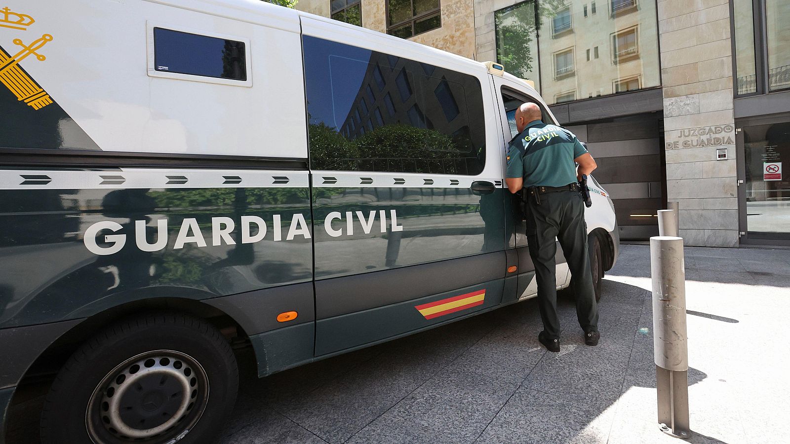 Agente de la Guardia Civil junto a una furgoneta aparcada frente a un edificio.  Se observa el texto "GUARDIA CIVIL" en el vehículo.
