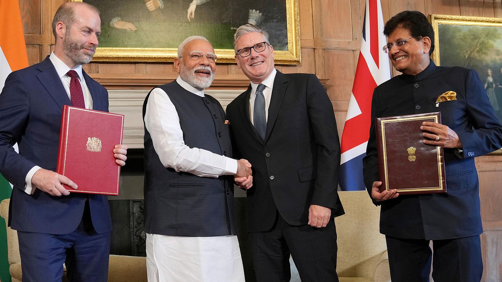 Firma de acuerdo entre Reino Unido e India. Narendra Modi, Primer Ministro de la India, estrecha la mano de un representante británico.  Presentes documentos del acuerdo.