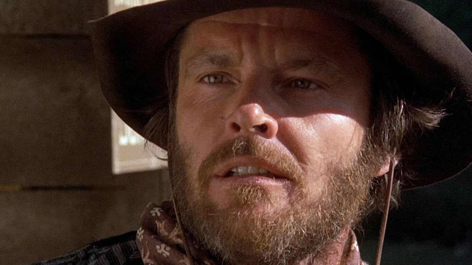 Clint Eastwood, primer plano con sombrero de vaquero y expresión seria.  Fotograma de película, iluminación que destaca las arrugas y textura de la barba.