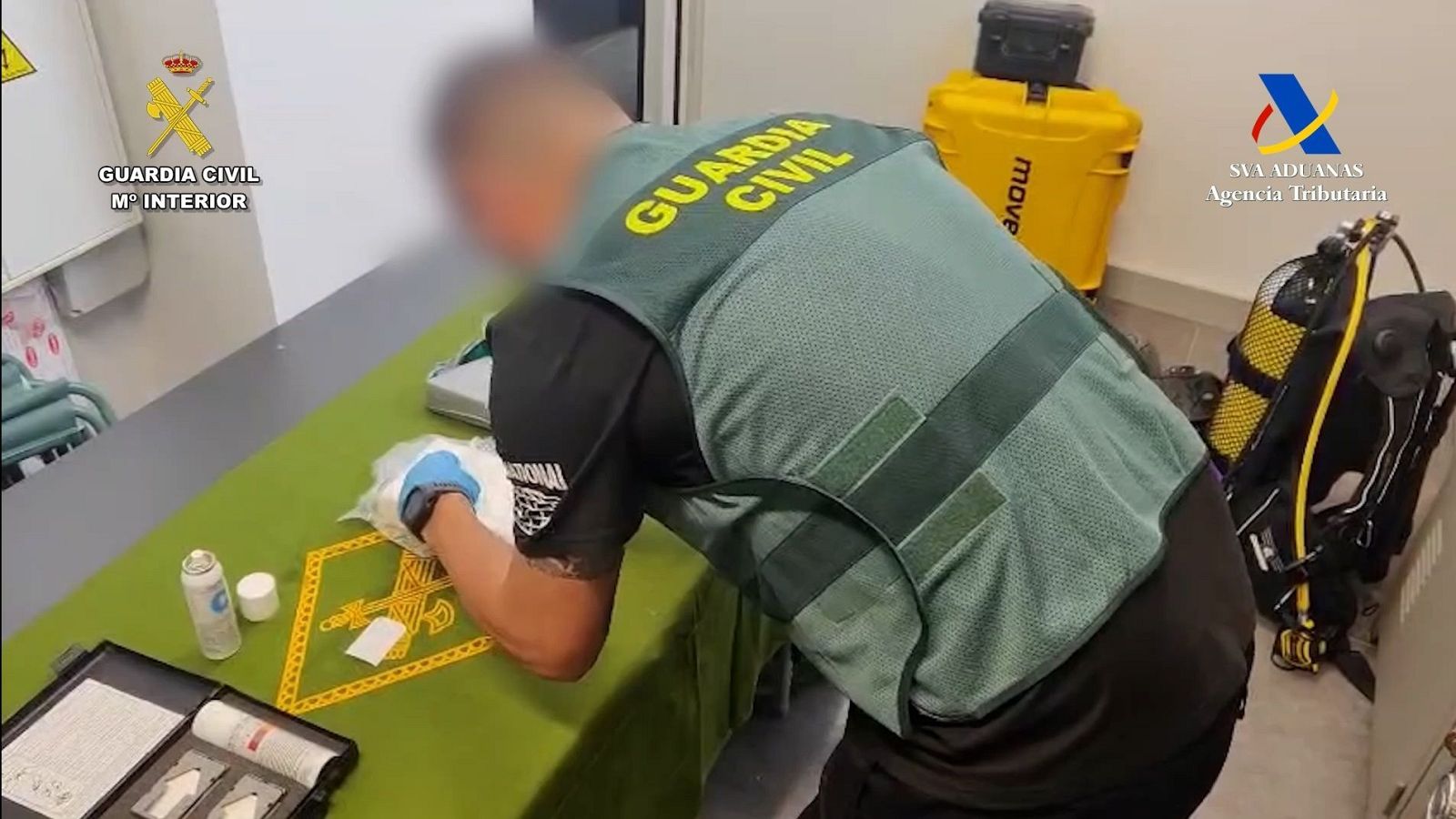 Agente de la Guardia Civil inspecciona evidencia (bolsas, kit de análisis) sobre mesa;  se observa equipo de buceo en la escena.