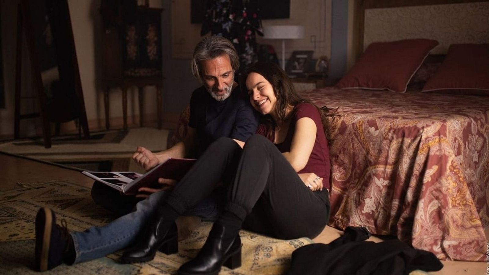 Escena de 'Un mundo normal' con Ernesto Alterio y Gala Amyach revisando un álbum de fotos, sentados en una habitación con decoración navideña.