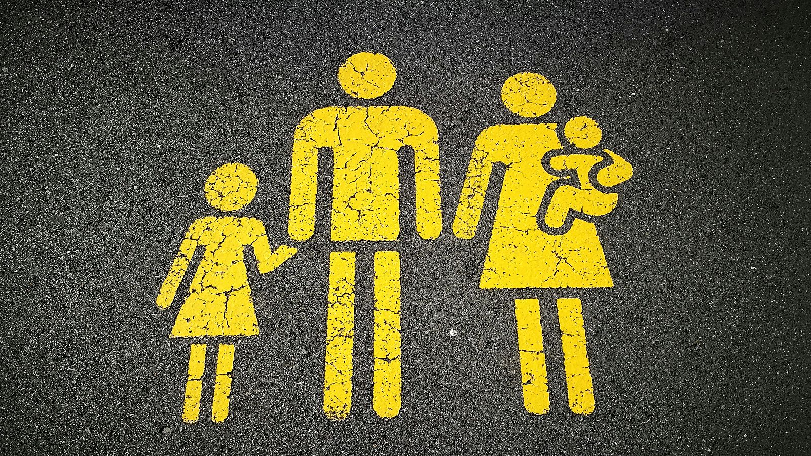 Pintura amarilla desgastada en asfalto, representando una familia (padre, madre con bebé y niña) con trazos simples.