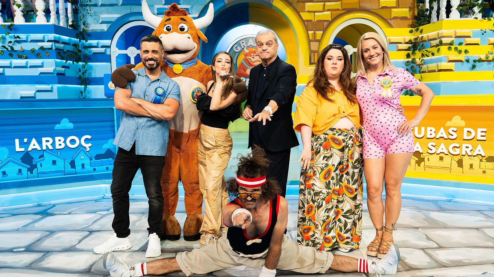 Ramón García presenta a los participantes del Grand Prix 2025, con atuendos vistosos y un escenario dividido en dos zonas con decoración de pueblos.