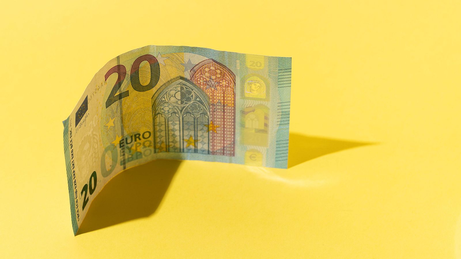 Billete de 20 euros doblado sobre fondo amarillo; el número 20 es visible en las esquinas; detalles arquitectónicos en el centro.